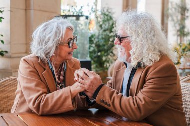 An affectionate elderly couple holding hands, basking in a delightful moment of love and connection, as they enjoy a romantic date filled with joy and warmth in the company of each other at a cozy