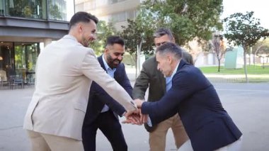 Four professional men in suits enthusiastically celebrating a recent achievement with a fun team gesture. They are expressing excitement and camaraderie in this lively business moment.