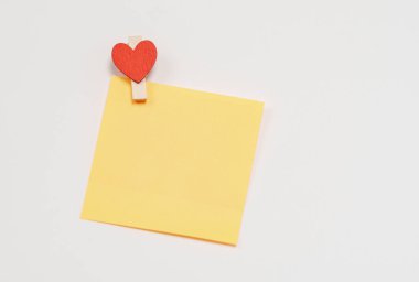 Turuncu kağıt notlar beyaz arka planda, tahta bir mandalla tutturulmuş kalp şeklinde..