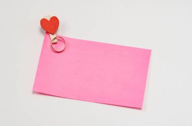 Pembe kağıt notlar, beyaz arka planda kalp şeklinde ahşap bir mandalla tutturulmuş..