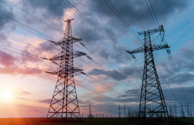 Güneş doğarken ya da batarken renkli bir gökyüzüne karşı yüksek voltajlı elektrik hatlarından oluşan bir siluet..