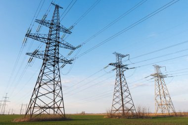 Yüksek voltaj hatları, pilonlar ve güneşli bir günde yeşil tarım arazisi. Bir fotoğrafta tarım ve endüstri derneği. Avrupa ovasının güzel bahar manzarası.