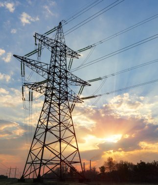Güzel bulutlu bir günbatımı gökyüzünün arka planında yüksek voltajlı elektrik hatları var. Güneş, elektrik direklerinin arkasında batıyor..