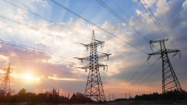 Güzel bulutlu bir günbatımı gökyüzünün arka planında yüksek voltajlı elektrik hatları var. Güneş, elektrik direklerinin arkasında batıyor..