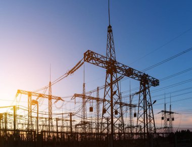 Güzel bulutlu bir günbatımı gökyüzünün arka planında yüksek voltajlı elektrik hatları var. Güneş, elektrik direklerinin arkasında batıyor..