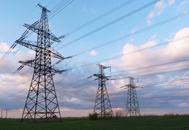 Güzel bulutlu bir günbatımı gökyüzünün arka planında yüksek voltajlı elektrik hatları var. Güneş, elektrik direklerinin arkasında batıyor..