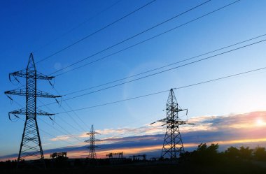 Güneş doğarken ya da batarken renkli bir gökyüzüne karşı yüksek voltajlı elektrik hatlarından oluşan bir siluet..