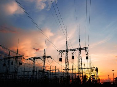 Güzel bulutlu bir günbatımı gökyüzünün arka planında yüksek voltajlı elektrik hatları var. Güneş, elektrik direklerinin arkasında batıyor..