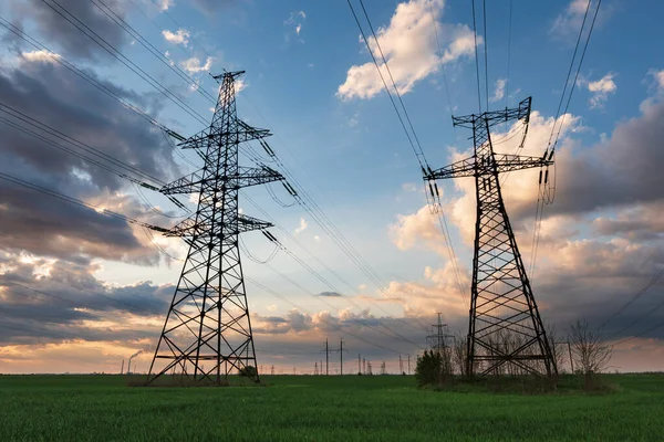 Günbatımında yüksek voltaj hatları, elektrik direkleri ve yeşil tarım manzarası. Bir fotoğrafta tarım ve endüstri derneği. Avrupa ovasının güzel bahar manzarası.
