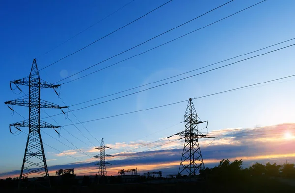 Güneş doğarken ya da batarken renkli bir gökyüzüne karşı yüksek voltajlı elektrik hatlarından oluşan bir siluet..
