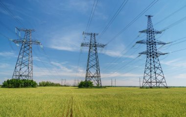 Yüksek voltaj hatları, pilonlar ve güneşli bir günde yeşil tarım arazisi. Bir fotoğrafta tarım ve endüstri derneği. Avrupa ovasının güzel bahar manzarası.