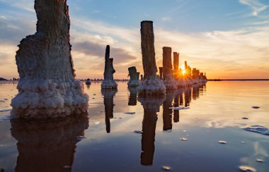 Ahşap direkler, Ukrayna 'da mavi gökyüzü ve tuzlu gölün pembe sularında tuz çıkarmak için bir kapı şeklinde eskimiş..