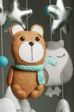 Sevimli bir ayı şeklinde keçeli bir oyuncak, çocuk arabasının bir parçası. Koyu gri bir arka planda. Çocuklar için yapılmış renkli ve çevre dostu çocuk cep telefonu.