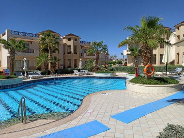 Lüks bir otelde palmiye ağaçlarıyla çevrili güneşli bir havuz..