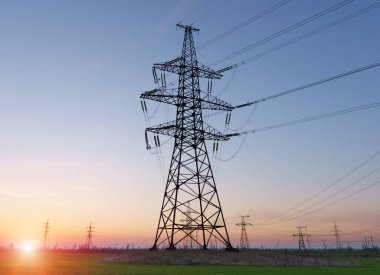 Yüksek voltaj hatları, elektrik direkleri ve güneş doğarken yeşil tarım arazisi. Bir fotoğrafta tarım ve endüstri derneği. Avrupa ovasının güzel bahar manzarası.