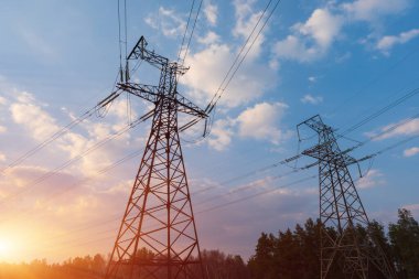 Güneş doğarken ya da batarken renkli bir gökyüzüne karşı yüksek voltajlı elektrik hatlarından oluşan bir siluet..