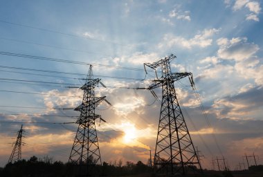 Güneş doğarken ya da batarken renkli bir gökyüzüne karşı yüksek voltajlı elektrik hatlarından oluşan bir siluet..
