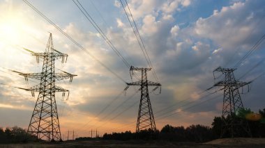 Güneş doğarken ya da batarken renkli bir gökyüzüne karşı yüksek voltajlı elektrik hatlarından oluşan bir siluet..