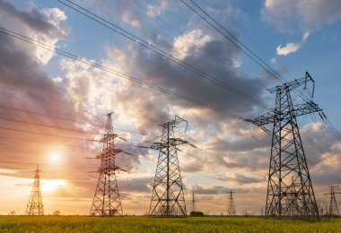 Güneş doğarken ya da batarken renkli bir gökyüzüne karşı yüksek voltajlı elektrik hatlarından oluşan bir siluet..