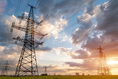 Güneş doğarken ya da batarken renkli bir gökyüzüne karşı yüksek voltajlı elektrik hatlarından oluşan bir siluet..