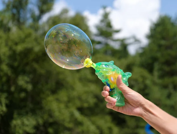 Gun for soapy bubbles in a female hand. Fun games with soapy bubbles on fresh air to the delight of children.