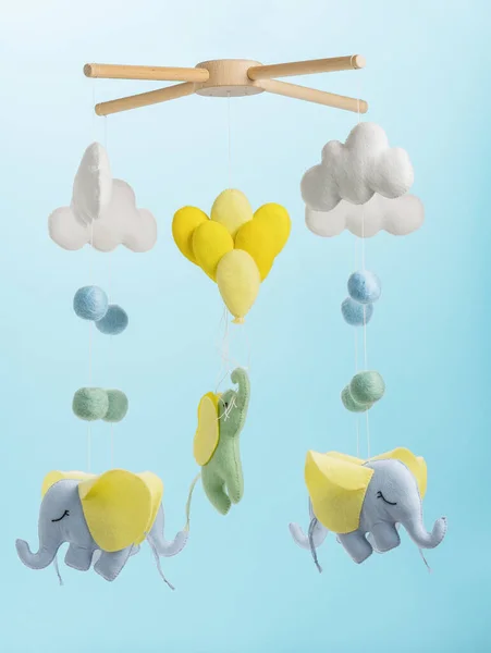 Colorful and eco-friendly children's mobile from felt for children. It consists of elephant, clouds and balloons toys. Handmade on blue background.