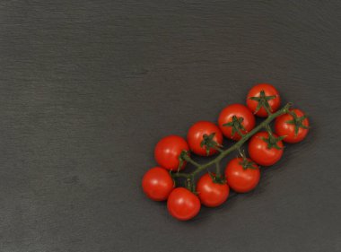 Koyu arkaplanda kırmızı kiraz domateslerinden bir dal. Küçük ve sulu sebzeler vitamin ve eser elementler açısından zengindir. Sağlıklı yiyecekler. Taze ve organik sebzeler. Çiğ yemek..