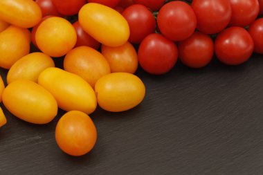 Saçılmış kırmızı ve sarı domatesler kayrak tabakasının karanlık yüzeyinde. Küçük ve sulu sebzeler vitamin ve eser elementler açısından zengindir. Sağlıklı yiyecekler. Taze ve organik sebzeler. Çiğ yemek..