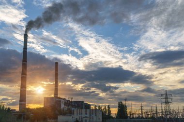 Güzel bulutlu bir günbatımı gökyüzünün arka planında yüksek voltajlı elektrik hatları var. Güneş, elektrik direklerinin arkasında batıyor..
