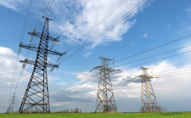 Mavi bulutlu gökyüzü ve yeşil çayır manzaralı elektrik direkleri.