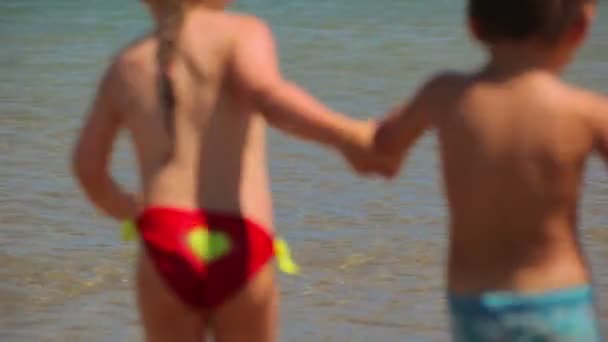 Kinderen lopen in het water op het strand — Stockvideo
