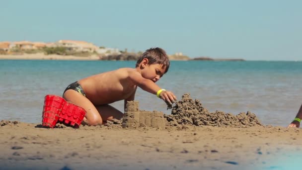O rapaz está a construir castelos de areia. — Vídeo de Stock