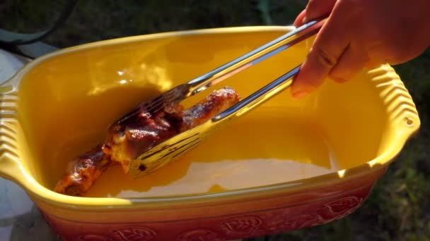 Hand med tång, placeras stekt kyckling ben i en keramisk maträtt — Stockvideo