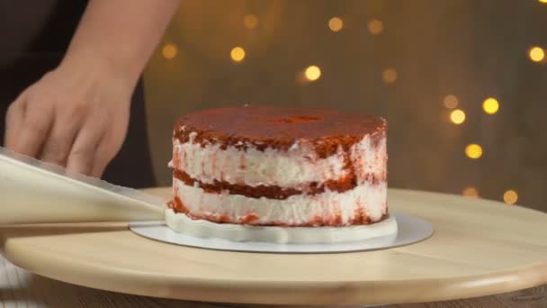 Кондитер украшает торт на стенде и со сливками — стоковое видео