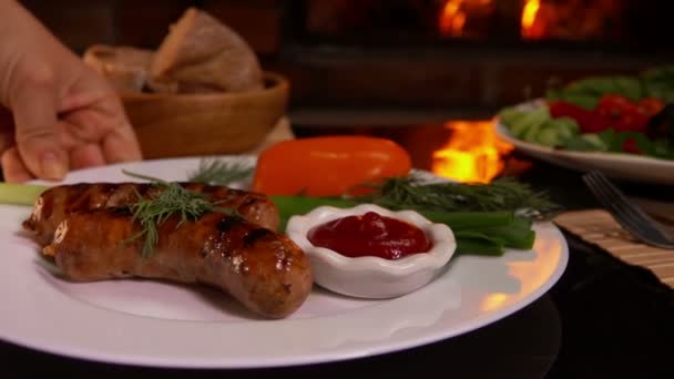 Hands put a plate of dinner with grilled sausage — Stock Video