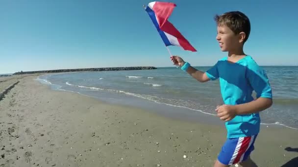 Chłopiec biegną wzdłuż plaży z flagą — Wideo stockowe