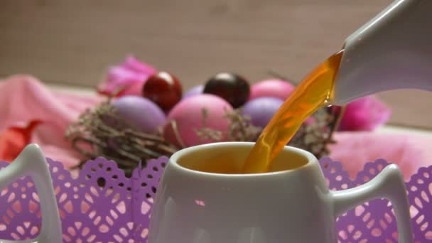 Кольорове рожеве великоднє яйце лежить. Чай наливають у чашку — стокове відео