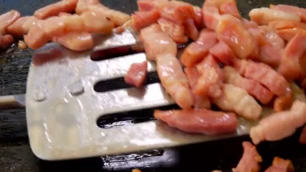 Metal spatula turns the diced bacon on the grill — Stock Video