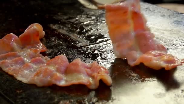 Cook turns bacon with metal tongs on the grill — Stock Video