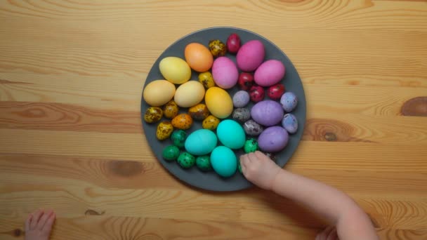 Barnens händer ta flerfärgad påsk ägg från en tallrik — Stockvideo