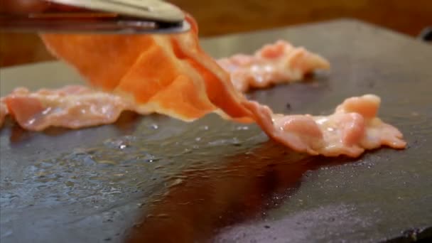 Cook turns bacon with metal tongs on the grill — Stock Video