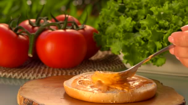 Lepel uitstrijkjes de saus op een broodje hamburger — Stockvideo