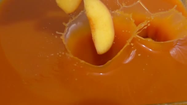 Кусочки персика попадают в сок — стоковое видео