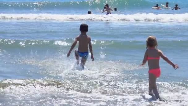 Τα παιδιά τρέχουν στο νερό στη γραμμή του σερφ. — Αρχείο Βίντεο
