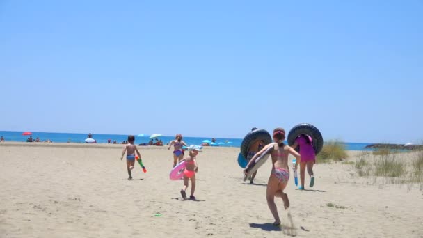 Gyermekek futnak a homokos tengerpart mentén a tenger — Stock videók