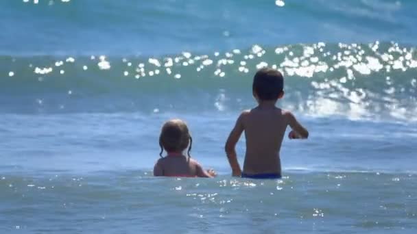 Niño y niña saltan sobre las olas — Vídeo de stock