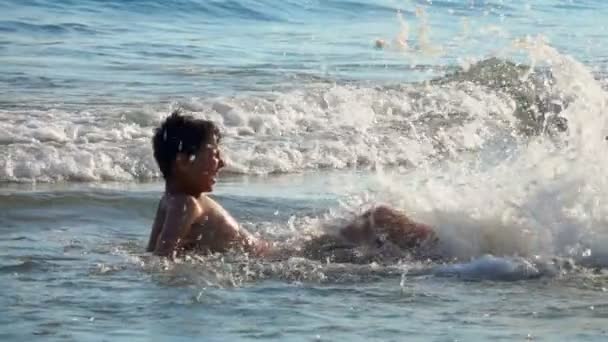 Jongen maakt spatten met voeten in het water op zee — Stockvideo