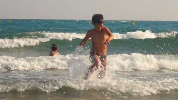 Wesoły chłopiec z rozpryskami biegnie na plażę. — Wideo stockowe