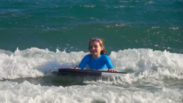 Petite fille glisse sur une vague sur une petite planche de surf — Video