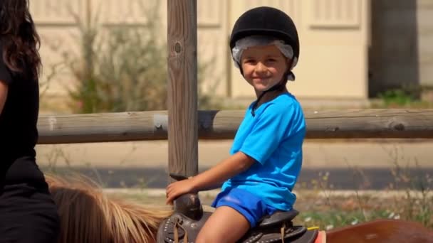 Petit garçon monte un poney et agite sa main — Video
